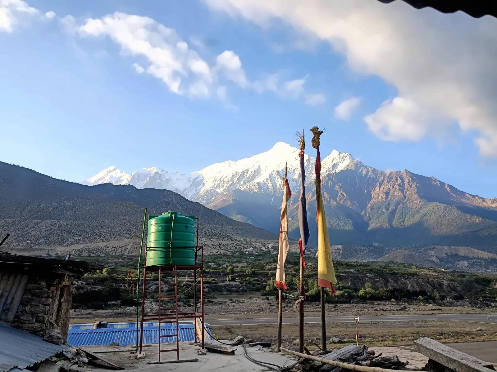 Nilgiri peaks above Jomsom with prayer flag poles and a rooftop water tank in the foreground