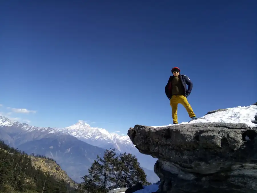 Govind Rai on a snowy rock ledge with Himalayan peaks behind at Kalinchowk, Dolakha